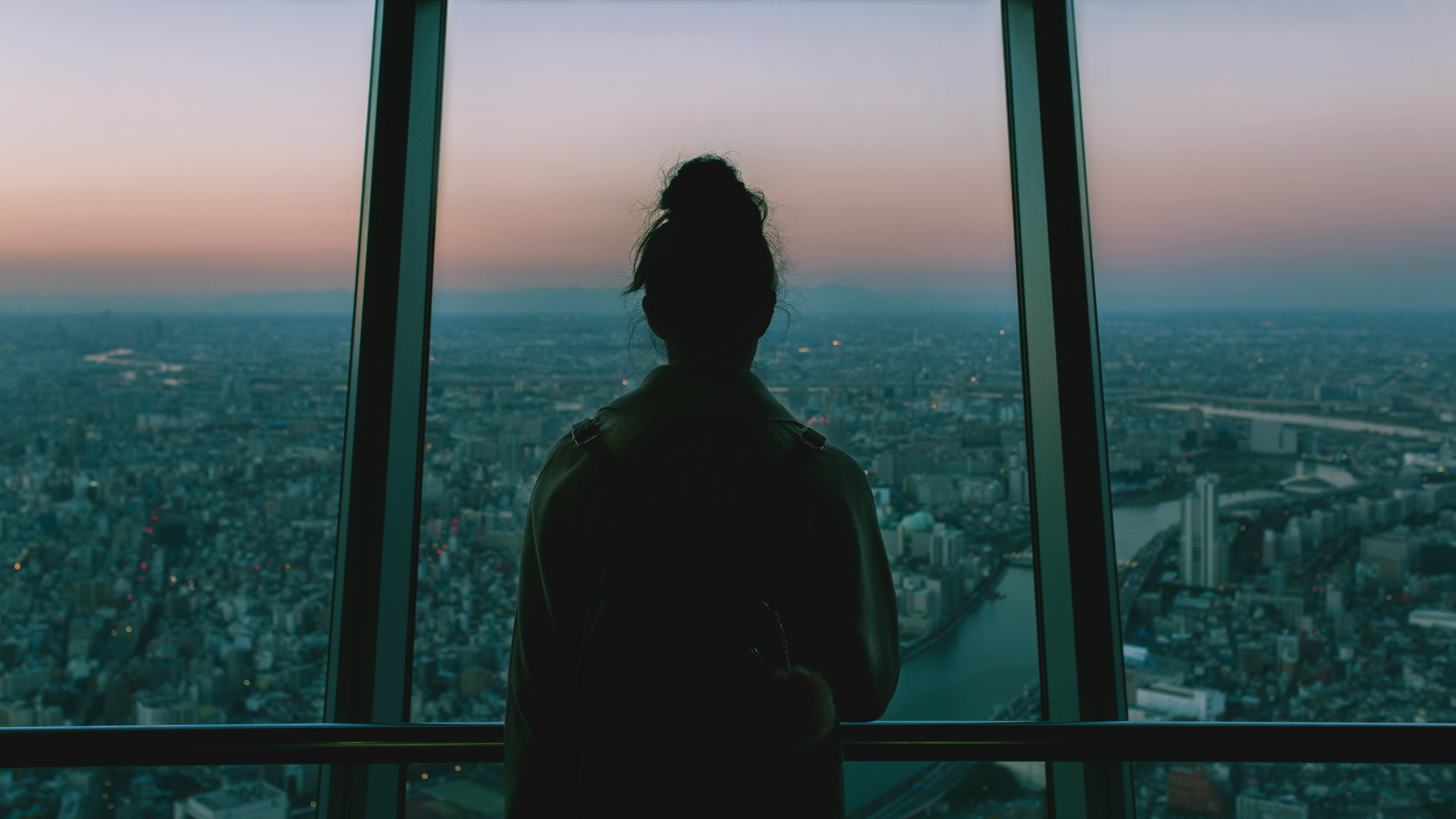silhouette of person standing inside the building facing the glass mirror watching the city